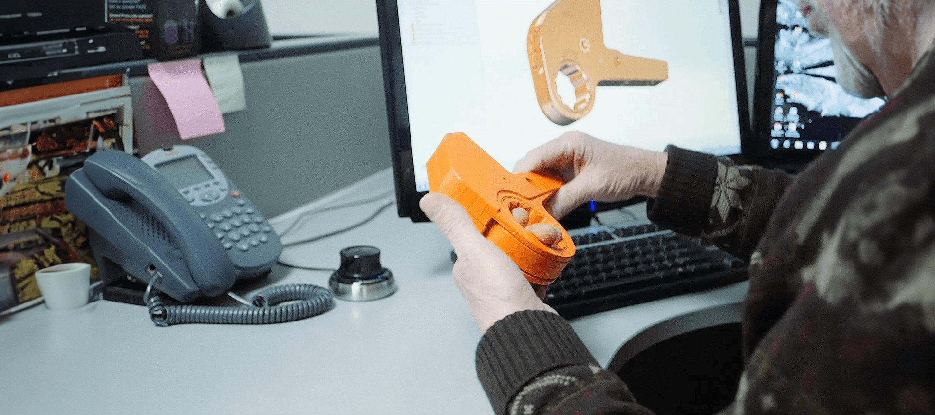 An engineer holding a 3D-printed custom tool prototype in front of a CAD model